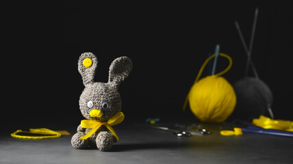 DIY Easter gift making theme. Handmade knitted toy Easter rabbit and needlework accessories. Black backdrop. Knitting concept. Dark moody style