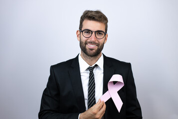 Young business man wearing suit holding a pink cancer ribbon over white background