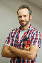 Patch up broken things. Portrait of cheerful handyman smiling at camera, standing with arms crossed and holding a hammer while posing indoors