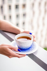 Hands holding cup of tea on the balcony. Cafe at home, quarantine concept