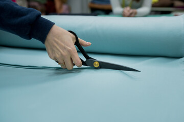 Closeup of seller cutting fabrics in textile store. Seamstress using scissors to trim the material...