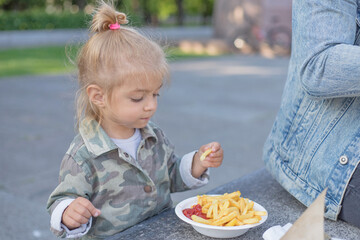 Little nice girl eating french fries with sauce at street outside.Concept of fast food and children.unhealthy food in childhood.