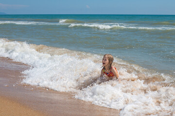 A child in a swimsuit laughs, splashing in the sea waves. Summer vacation at the sea
