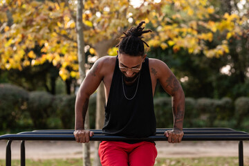 african american athlete boy does calisthenics fitness exercises on bars in park