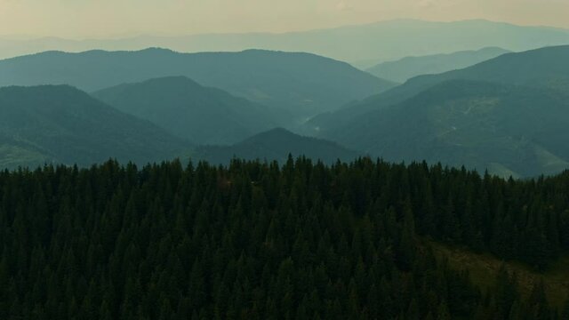 Aerial view of sunrise in the misty forest. Foggy sunset in mountains. Flying over green trees. Morning mist, country fields, sun rising over the horizon layers. Mysterious nature landscape.