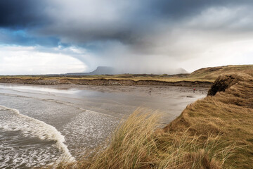 Rosses point beach and Benbulben flat top mountain covered in snow in county Sligo, Ireland, Warm sunny day, cloudy blue sky covers the peak of the mountain.