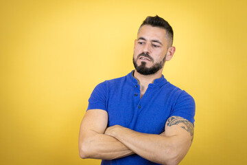 Fototapeta premium Handsome man with beard wearing blue polo shirt over yellow background thinking looking tired and bored with crossed arms