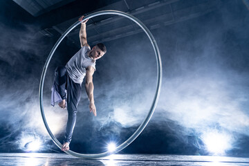 Cyr Wheel circus artist on smoked, dark background performing on stage 