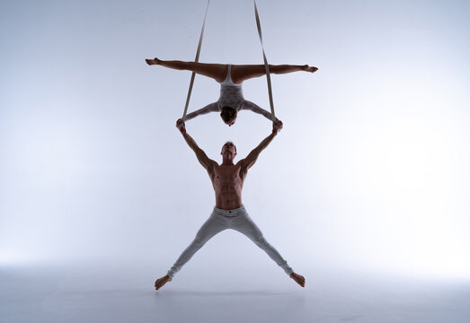 Aerial straps duo wearing white costume on white background doing performance 