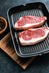 Raw New York striploin beef steak on black grilling pan with chili pepper, top view.