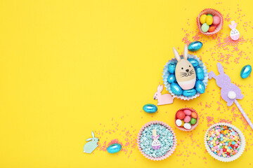 Easter concept. Sweet eggs with sprinkles and decorative rabbits on yellow background