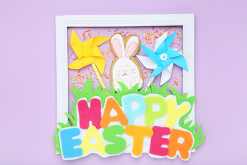 Text Happy Easter with rabbit cookie and paper windmills on purple background
