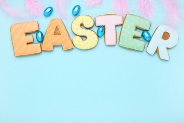 Word Easter by cookies with eggs and pink feathers on blue background