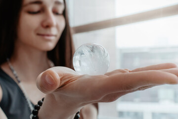 Woman in grey clothes smiles and holds in her hands semiprecious sphere , object for religious rituals, meditations and alternative medicine. Girl looks at amazing mineral ball