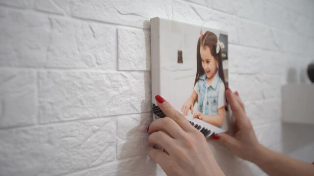 Side view happy young woman putting photo on fireplace, decorating living room. Smiling female homeowner enjoying improving interior, making apartment cozy. moving concept. woman hangs photo canvas