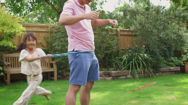 Asian father and daughter having fun playing with hula hoop in garden at home =- shot in slow motion