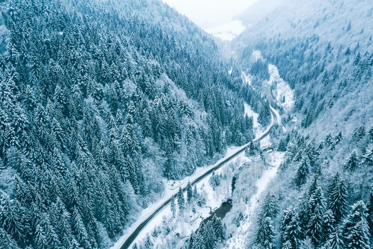 Aerial top view drone shot of the pine and spruce trees forest covered with snow in the Tatra Mountains in Slovakia with a countryside rural road. Transportation and ecology concept image.