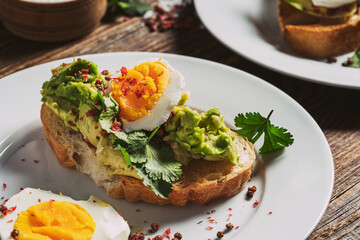 Poached egg and avocado  on sliced toasted bread, two plates, top view