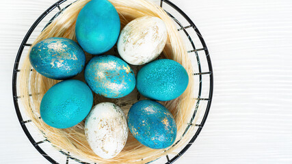 Basket with Easter colored eggs close-up top view in scandinavian loft style. An original element for modern Easter design. Blue, turquoise with gold eggs for Easter decor.