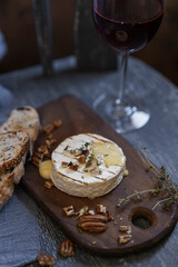 Baked on grill camembert or brie cheese with bread toasts, nuts, herbs and fruit jam with glass of red wine, textured grey rustic background, selective focus, copy space