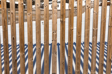 Wooden fence in the village on a winter sunny day. Game of shadows of a wooden fence in a winter landscape.