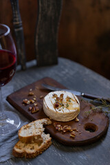Baked on grill camembert or brie cheese with bread toasts, nuts, herbs and fruit jam with glass of red wine, textured grey rustic background, selective focus, copy space