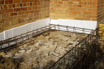 Reinforcement frame is placed in trench and is adjacent to the old house. Close-up. New reinforcement cage and old foundation are separated by foam sheets.