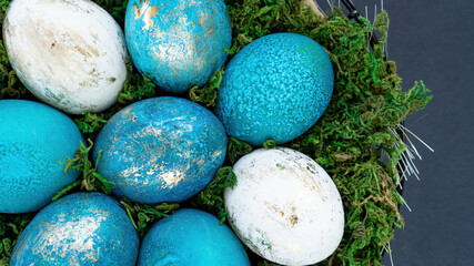 Easter eggs close-up top view. Easter background with colored turquoise and gold eggs in a nest basket with forest moss on a black background with copy space. Trendy idea for the modern Easter design.