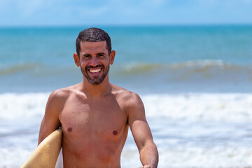 HOMEM DE 30 ANOS SAINDO DO MAR COM UMA PRANCHA DE SURF, GUARAPARI, ES, BRASIL.