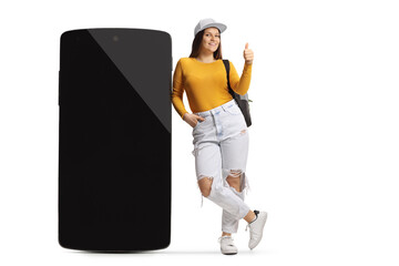Young female leaning on a big smartphone and showing thumbs up