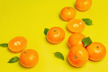 Ripe juicy tangerines and fresh leaves on yellow summer background
