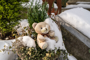 kleiner Teddyb&auml;r halb vom Schnee bedeckt neben einem Grabstein