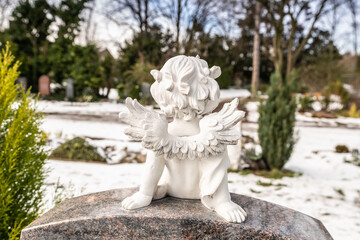 Kleiner Engel von hinten auf einem Grabstein mit Schnee im Hintergrund