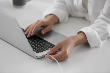 Woman connecting charger cable to laptop at white table, closeup