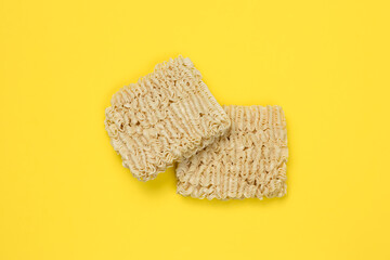 Instant noodles, ramen, dried noodle blocks on a yellow background. Unhealthy food concept. Uncooked pasta. Top view. Traditional Japanese cuisine.