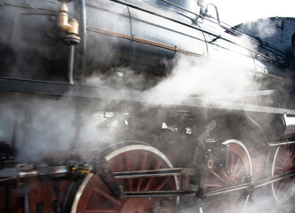 Steam rises from the boiler above the steel wheels of a vintage locomotive in Novara, Italy.