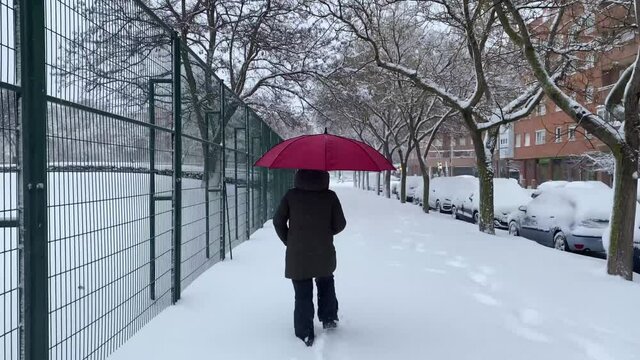 Woman with red umbrella walking near a completely snowy park.
