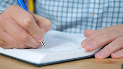 Close up hands businessman owner CEO director boss sitting on chair at table writes to-do list in notebook works at home office. Business man top manager freelancer writes information notepad with pen