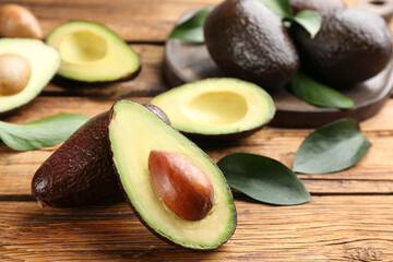 Whole and cut avocados with green leaves on wooden table, closeup