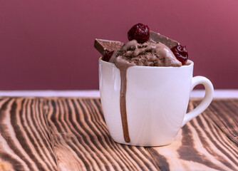 pudding with ice cream, cherries and pieces of chocolate in a mug on a jjon wood table. Melted ice cream flows in a mug on a pink background. High quality photo