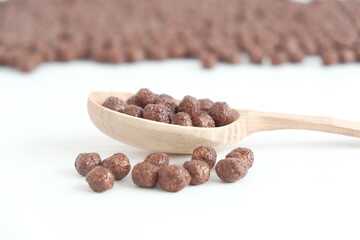 Chocolate corn balls in a wooden spoon scattered on a white background. Copy, empty space for text