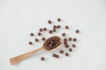 Chocolate corn balls in a wooden spoon scattered on a white background. Top view. Copy, empty space for text