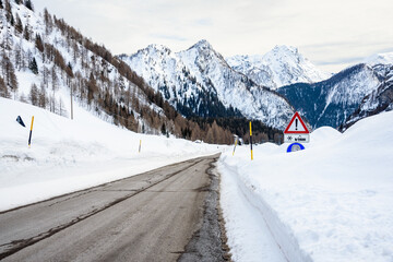Warning traffic sign in deep snow along a deserted mountain road in the European Alps on a cloudy winter day