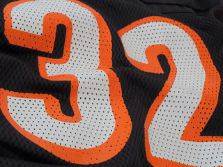 Orange and white numbers display 32 up close on a black mesh sports jersey.