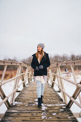 A woman walking across a snowy bridge dressed in cold weather gear 