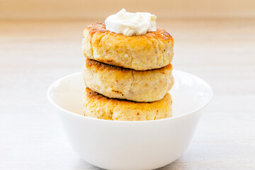 Homemade cottage cheese pancakes syrniki stack on round glossy white bowl on white rustic natural wooden table background. Close up. Selective focus. Copy space