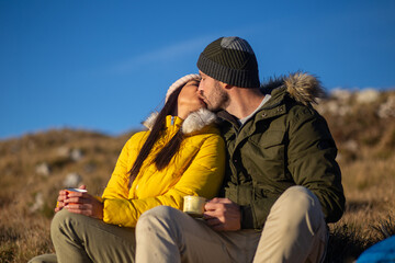 Fototapeta premium Happy couple sitting and kissing at the mountain. 