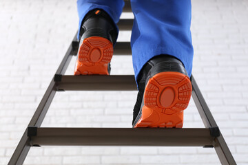 Professional worker climbing up ladder against white brick wall, low angle view