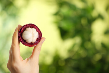 Woman holding open mangosteen fruit outdoors, closeup. Space for text