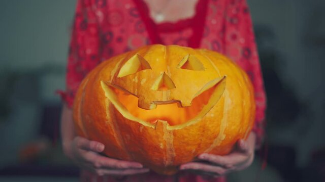 a woman is holding a large pumpkin with eyes and mouth carved out, and a candle is burning inside the pumpkin. the concept of fear at the Helluin holidays